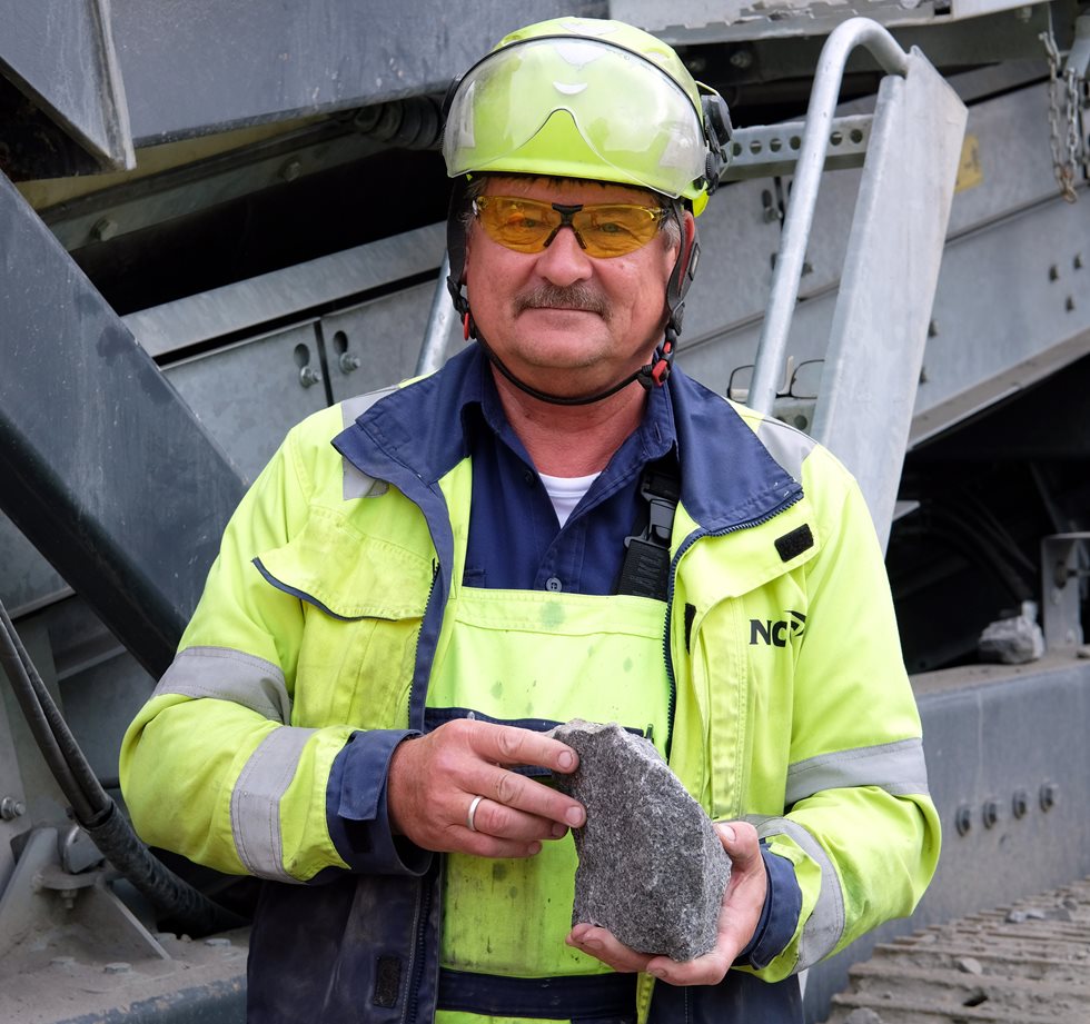 A man holding a rock in front of a Lokotrack.