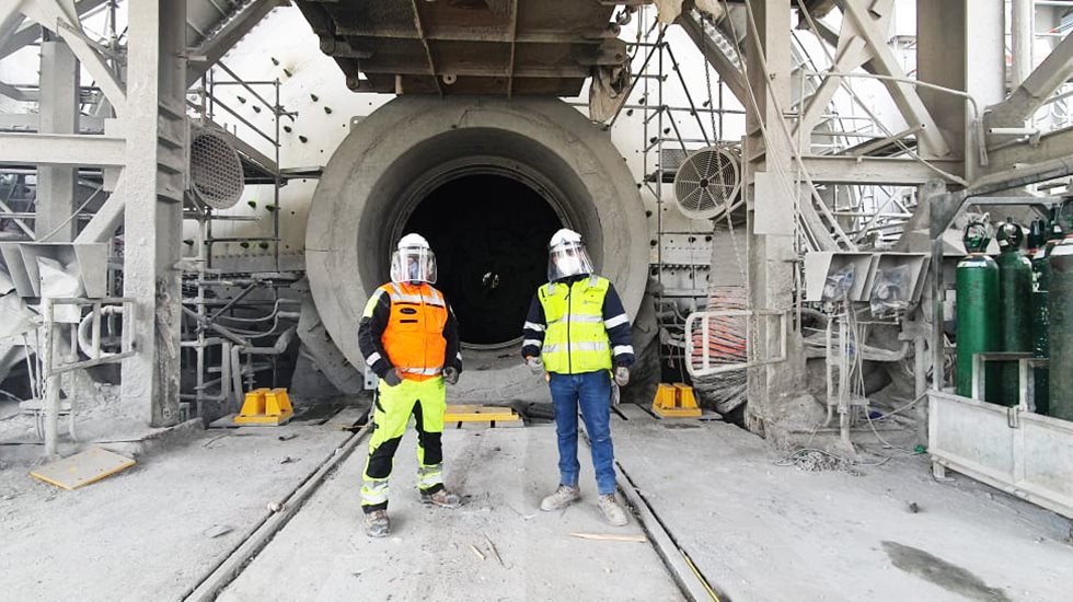 Two men in front of ball mill opening.