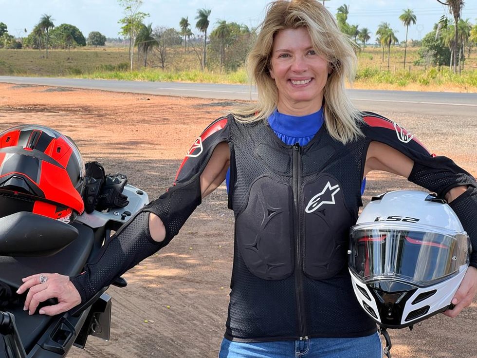 Paula Peres next to a motorcycle, holding a helmet.